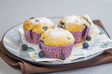 Pripravljeni borovničevi skutini kolački v pekaču za muffine, okrašeni s svežimi borovnicami.