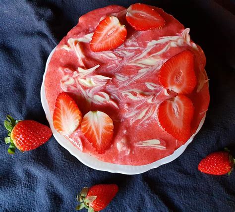 Sestavljena jagodna tortica v tortnem modelu, s plastmi piškotnega dna, jagodnega pireja in skutne kreme.