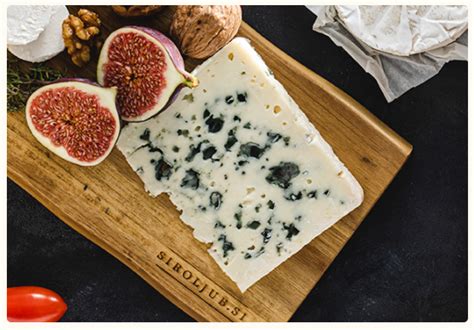 Različni siri z modro plesnijo na leseni deski, obdani z orehi in grozdjem.