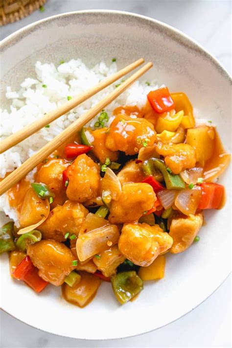 Pripravljen piščanec v sladko-kisli omaki, postrežen s kuhanim rižem in okrasom.