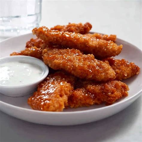 Photo of golden brown fried chicken strips with sesame seeds, served in a casual setting.