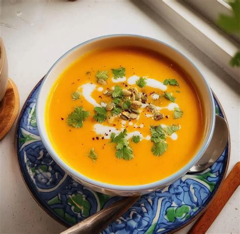 Thematic photo of a bowl of carrot and ginger soup, garnished with herbs