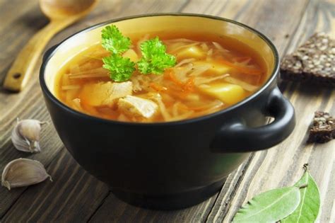 Tradicionalna ruska juha šči v keramični posodi, postrežena s kislo smetano in svežimi zelišči.