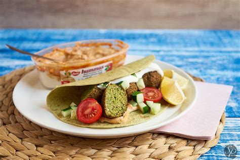 Ilustracija pripravljenih lečinih polpetov, postreženih na tortilji s humusom, špinačo in čilijem.