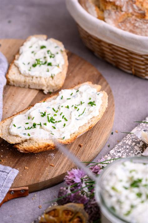 Zeliščni skutni namaz v skledi, obkrožen s svežim drobnjakom, peteršiljem in rezinami kruha