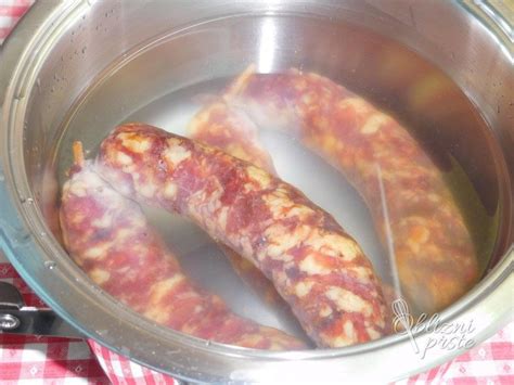 Prikaz prekajenega svinjskega vratu v loncu med kuhanjem, z jasno vidno vodo in začimbami.