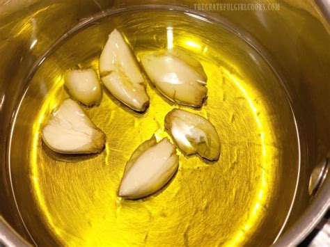 A picture of garlic cloves in olive oil in a saucepan, slowly cooking.
