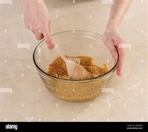 The process of mixing crushed biscuits, melted butter, and sugar in a bowl, then pressing the mixture into a square baking pan.
