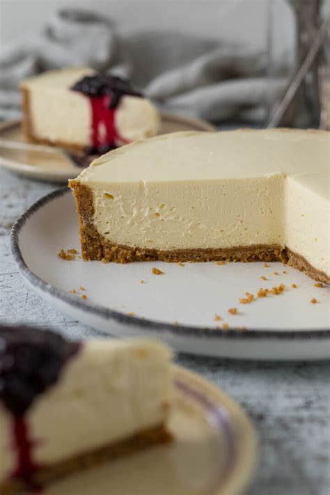 A beautifully presented slice of a three-layered baked dessert, showing a biscuit base, a creamy cheese filling, and a smooth sour cream topping, garnished with fresh berries.