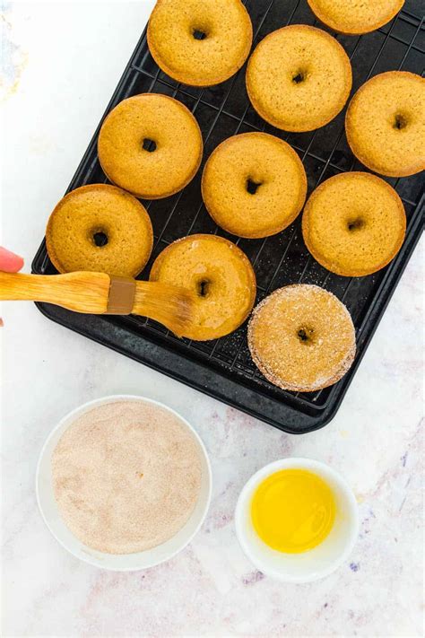 Photo of baked donuts on a baking tray, being brushed with melted butter.