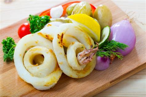Thematic photo of fresh squid on a wooden board with lemons and herbs