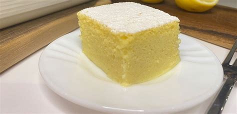Sveže pripravljeno limonino pecivo, posuto s sladkorjem v prahu, s svežimi rezinami limone v ozadju.