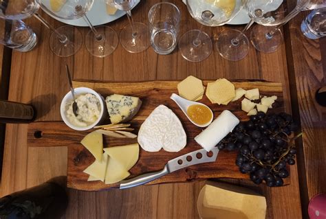 Tematska fotografija: razrezan sir prosenik na leseni deski, zraven marmelada, oreščki in kozarec vina