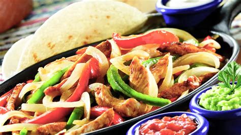 Tematsko foto: piščančje fajitas v ponvi, pripravljene za serviranje s tortiljami in omakami