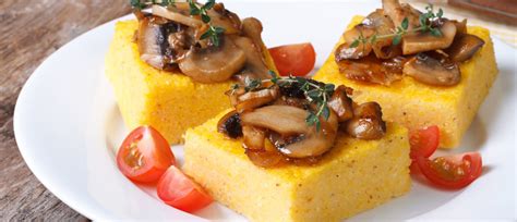 Pripravljena pečena polenta, narezana na kocke in obložena s paradižnikom in zelišči.