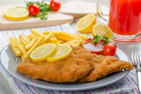 Thematic photo of a crispy Viennese schnitzel (Dunajski zrezek) with lemon slice and a side of french fries