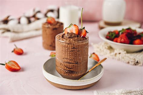 Pripravljen čokoladni veganski mousse v kozarcih, okrašen z malinami ali meto.