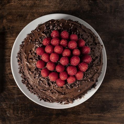 Presna torta z več plastmi, okrašena s svežimi malinami in čokoladnim prelivom