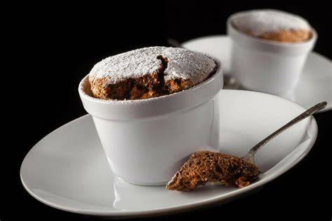 Temno čokoladni sufle, ki se dviguje iz skodelice, posut s sladkorjem v prahu