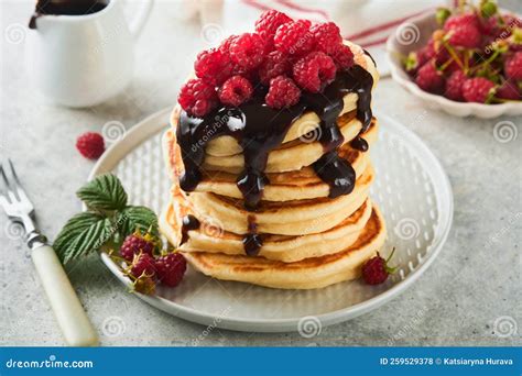 The image should show a beautifully stacked plate of American pancakes with melted chocolate, sliced bananas, and raspberries.