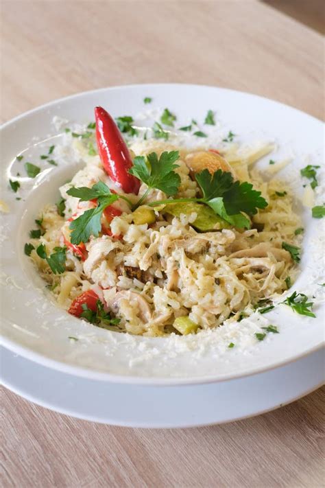 Thematic photo of a creamy risotto dish with chicken and vegetables, garnished with fresh herbs.