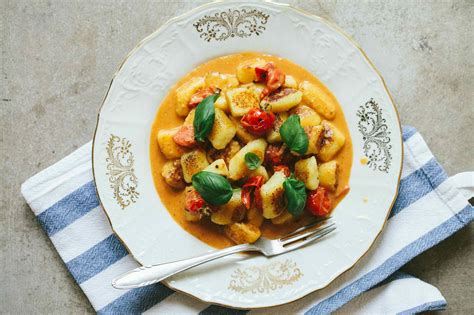 Fotografija pečenih njokov s češnjevimi paradižniki, česnom in zelišči na pekaču.