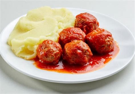 Fotografija krožnika s švedskimi mesnimi kroglicami, pire krompirjem, brusnično omako in vloženimi kumaricami